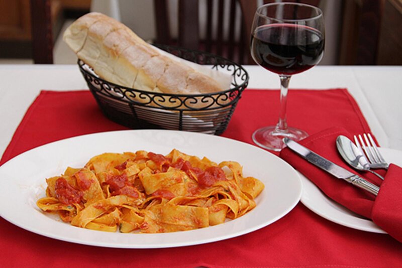 Pappardelle pasta entree with a glass of red wine and a basket of bread