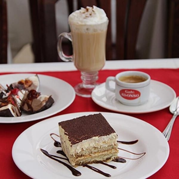 Dessert spread with tiramisu, chocolate-covered ice cream, a latte, and espresso on a red placemat.