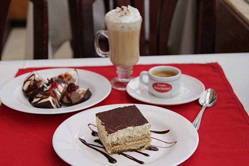 Dessert spread with tiramisu, chocolate-covered ice cream, a latte, and espresso on a red placemat.