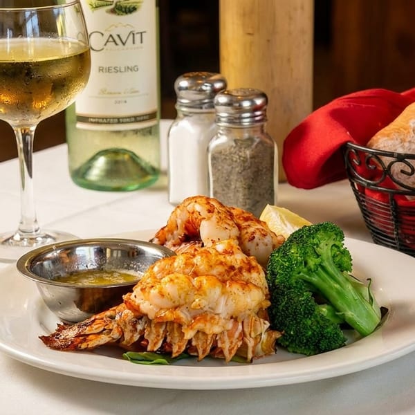 Lobster tail and shrimp with broccoli, drawn butter, white wine, and bread on a white tablecloth.