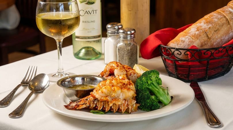 Lobster tail and shrimp with broccoli, drawn butter, white wine, and bread on a white tablecloth.
